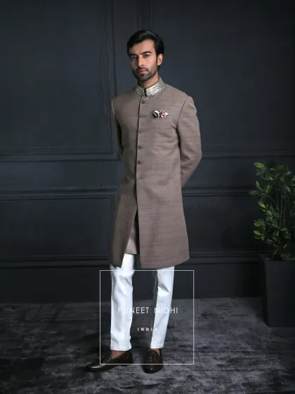 Tailored in earthy brown matka silk, this achkan embodies understated luxury. A paisley-embroidered stole in antique metallic threads adds regal charm, balanced with modern ivory trousers.