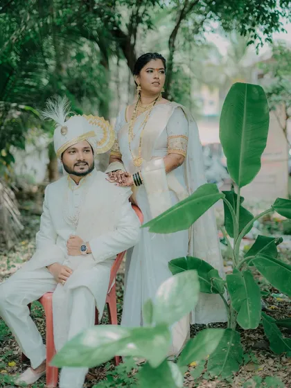 A stylish portrait of the couple in their white traditional outfits. The composition with the large green leaves adds a natural and artistic element to the photo.