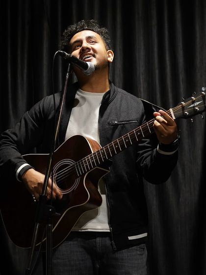 A singer and guitarist in his element during a performance. The dark background and focused spotlight create a professional and intimate setting for our musical acts.