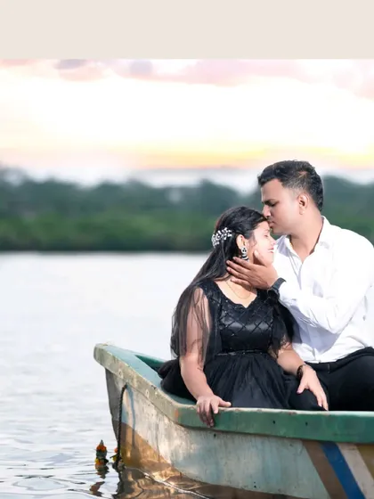 A tender moment captured during a pre-wedding shoot, with the groom kissing the bride's forehead as they sit in a small boat on a calm lake.