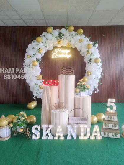 A white and gold themed stage decoration with a balloon ring, neon sign, and multiple props.
