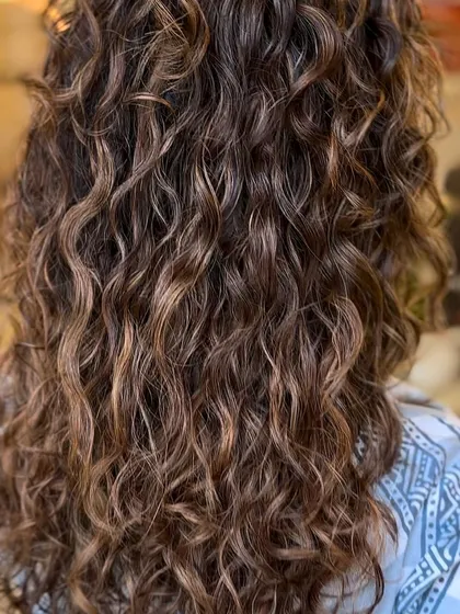 A brunette balayage on curly hair. The highlights are carefully placed to enhance the natural curl pattern and create beautiful dimension.