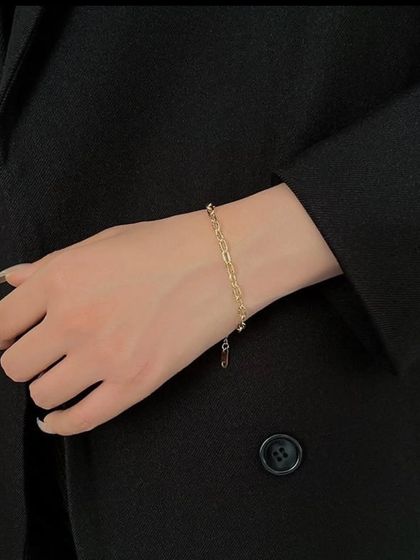 A fine paperclip chain bracelet, shown here adding a subtle touch of modern elegance to a classic black blazer. It's lightweight and comfortable for all-day wear.