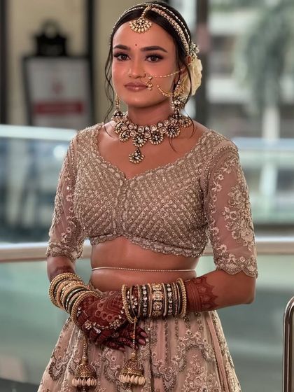 A full view of the bride in her elegant beige lehenga, her hair styled in a classic floral bun.