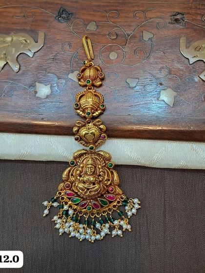 This lightweight maang tikka is made from hallmarked 92.5 silver with gold plating. It features a Goddess Lakshmi motif and is adorned with colorful stones and pearl drops.