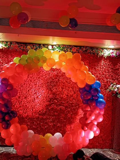 The rainbow balloon ring backdrop for a birthday, seen here under red ambient lighting, creating a dramatic effect for evening celebrations.