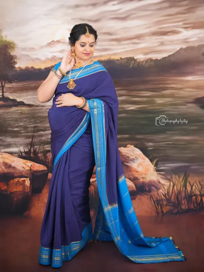 A beautiful studio portrait of a mother-to-be in a blue saree, set against a painted backdrop of a serene landscape.