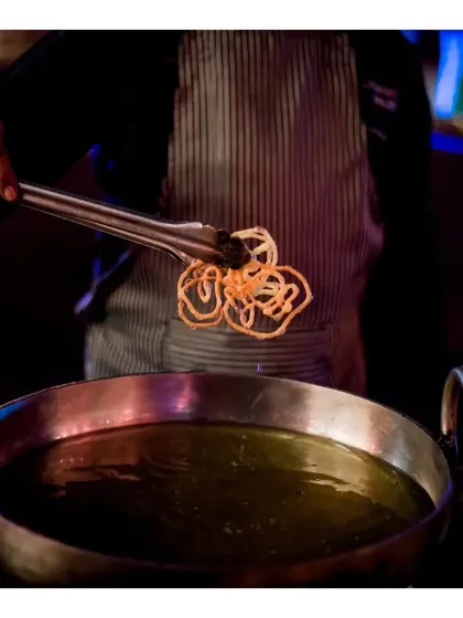 A chef carefully lifts a freshly fried, crispy nano jalebi from the hot oil at our live dessert station.