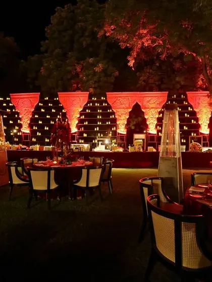 A wide view of the outdoor dining area, with tables dressed in red and lit by heaters and candles, creating a warm and inviting space under the trees.