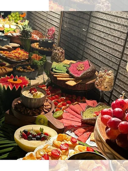 Our grazing tables are a feast of textures and colors. This setup features a variety of dips, crackers, cheeses, and carved fruits, all arranged with tropical leaves to create a lush and inviting look.