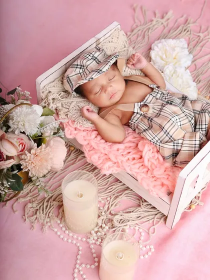 A classic and adorable look for a baby boy, dressed in a plaid romper and cap, sleeping peacefully in a tiny wooden bed.