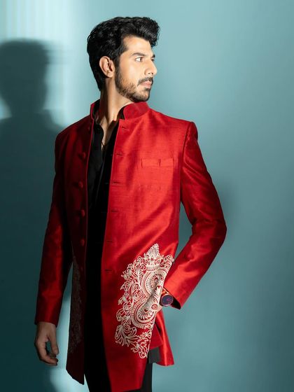 A three-quarter shot showcasing a modern Indian wear look. The vibrant red jacket provides a strong pop of color.