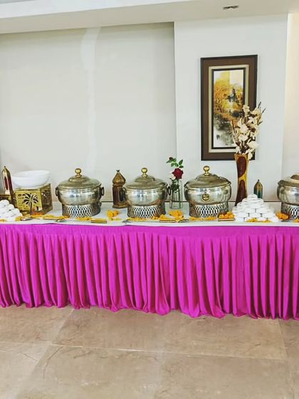 A bright and festive buffet setup with a vibrant pink table skirt, perfect for celebrations like birthdays or roka ceremonies.