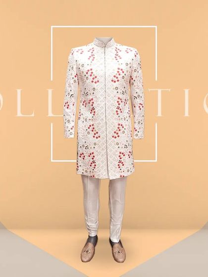 A full-length view of the cream sherwani with red floral embroidery. Paired with a white churidar and traditional juttis, this outfit embodies elegance and is ready for any grand wedding celebration.
