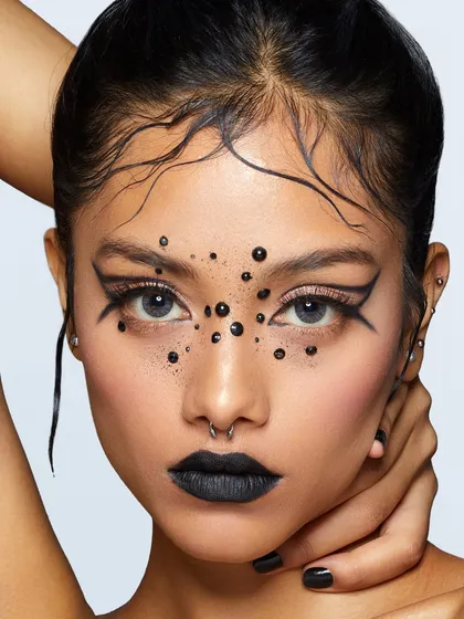 A dark, edgy look with black lipstick, graphic liner, and black dot embellishments for a dramatic, punk-inspired aesthetic.