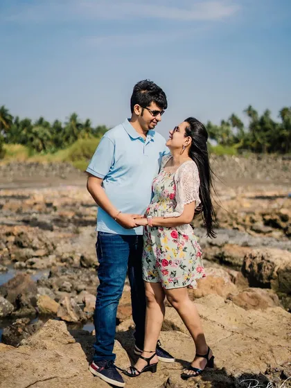A happy couple posing on the rocks by the sea, a perfect example of a daytime beach pre-wedding photo.