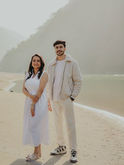 A couple stands on the sandy banks of the Ganga, their white outfits creating a serene and pure look.