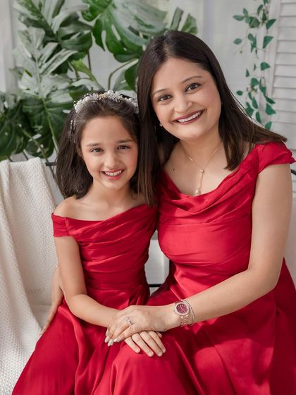 A classic and elegant portrait of a mother and daughter in beautiful red gowns.