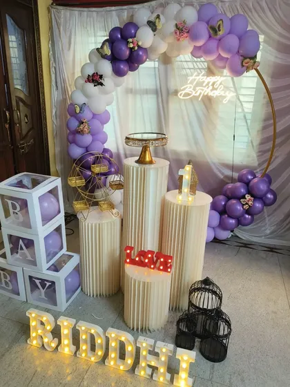 A lovely purple and white balloon ring for a first birthday, accented with delicate butterfly details, a neon sign, and matching balloons in the 'B-A-B-Y' blocks.