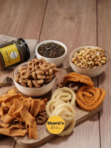 Welcome to my snack-arena. This board features a variety of my crunchy snacks like Kodbale, Ribbon Murukku, and peanuts, paired with my special homemade chutney. It's a perfect platter for sharing with loved ones.