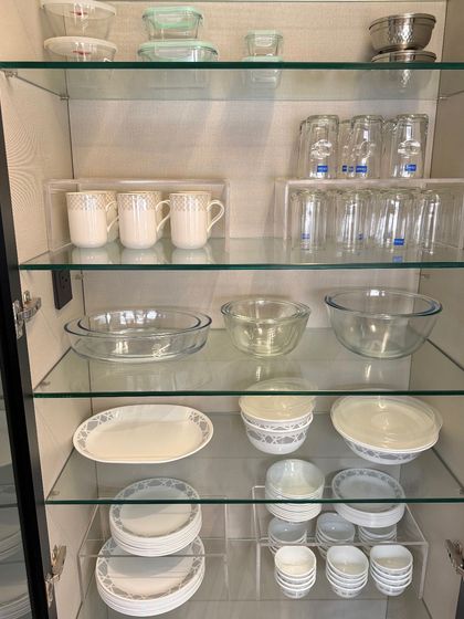A glass-front cabinet organized with Corelle dinnerware, glassware, and serving bowls. We use acrylic risers to create clean lines and make everything visible.