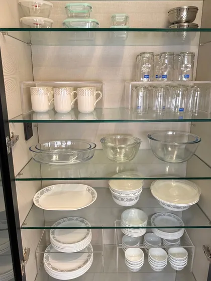 A glass-front cabinet organized with Corelle dinnerware, glassware, and serving bowls. We use acrylic risers to create clean lines and make everything visible.