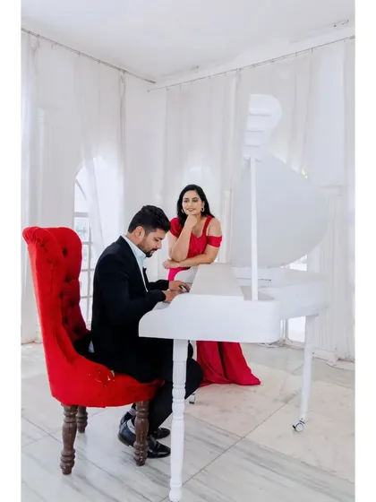 A creative studio pre-wedding shoot with a white piano and a dramatic red chair, creating a scene that is both classic and modern.