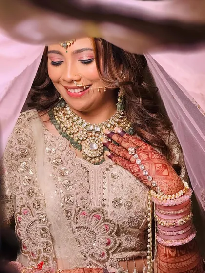 A peek-a-boo shot of a bride under her veil. She is wearing an elegant ivory lehenga with a heavy polki and kundan necklace, a perfect blend of modern color and traditional craftsmanship.