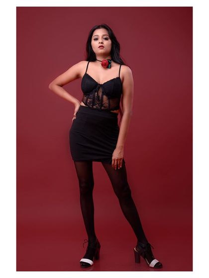 A full-body shot of a model in a black dress against a red background. The pose is strong and confident, creating a classic and powerful fashion statement.