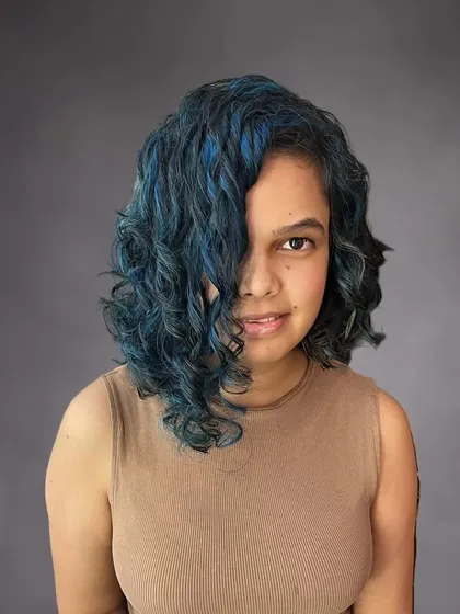 For clients who want to make a statement, I love creating bold, creative looks. I gave Nikita's curly hair an edge with an asymmetrical bob and hand-painted vibrant blue highlights that really pop against her dark hair.