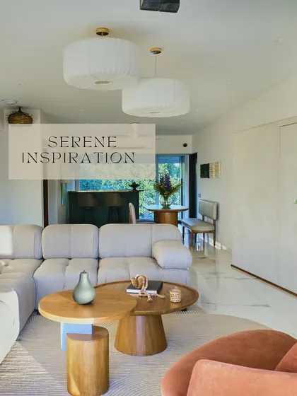 An open-plan living space designed for serenity and flow. The large, comfortable sectional sofa, paired with organic-shaped wooden coffee tables and soft, pleated pendant lights, creates a cohesive and tranquil environment.