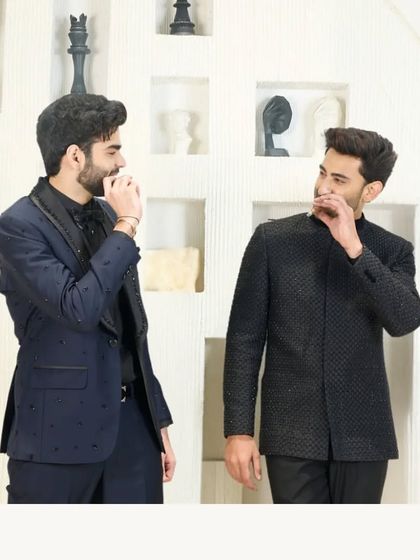 Two gentlemen in complementary evening wear. One wears the navy blue tuxedo with beaded lapels, while the other dons a textured black Jodhpuri jacket, showcasing different facets of my formal collection.