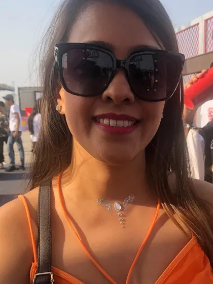 A smiling client showing off her finished glitter necklace tattoo. It's a perfect accessory for a sunny festival day.