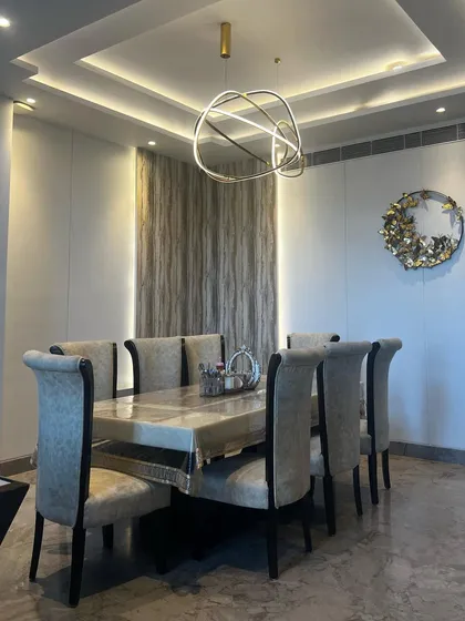 This dining space features a striking accent wall with wood-textured wallpaper, flanked by vertical strip lighting for a dramatic effect. The design is anchored by a modern chandelier and a substantial eight-seater dining table, creating a sophisticated and well-defined area.