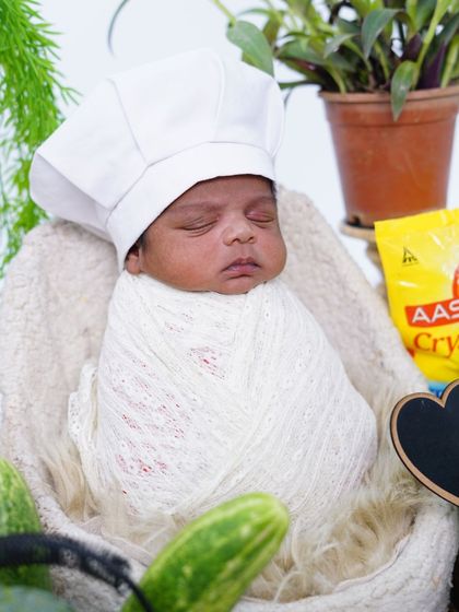 A close-up of the newborn chef, sleeping peacefully in his little chef hat. The details, like the bag of flour and fresh cucumbers, make the theme authentic.