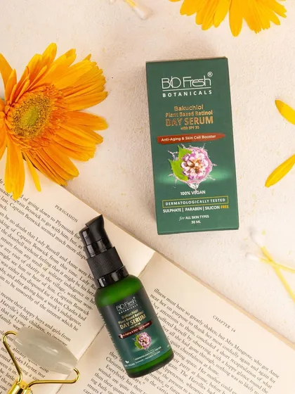 A lifestyle flat lay of Biofresh Botanicals' day serum, styled with a book, flowers, and a face roller. This composition suggests a relaxing, intellectual, and mindful self-care routine.
