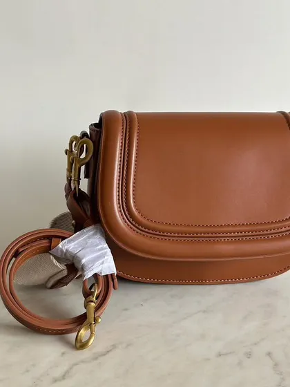 A close up of the brown Noble bag with the long leather strap ready to be attached. You can see the quality stitching and the smooth finish of the leather.
