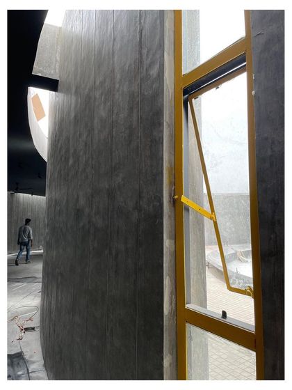 A bright yellow window frame installed against the textured concrete wall of the memorial gallery.