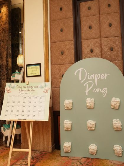A game corner featuring 'Diaper Pong' and a 'Guess the Date' calendar. These interactive elements are designed to match the event's soft green and neutral theme.