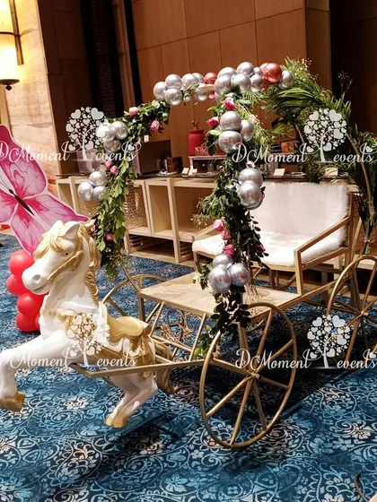 A magical baby entry carriage for a winter wonderland or princess party. The white and gold carriage is adorned with greenery, silver balloons, and a large pink butterfly prop.