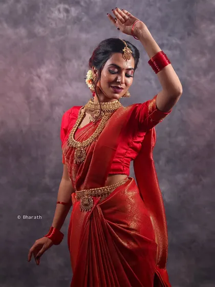 A dynamic pose in a traditional red saree, highlighting the flow and grace of the fabric. This studio shot for a bridal portfolio captures a sense of movement and celebration.