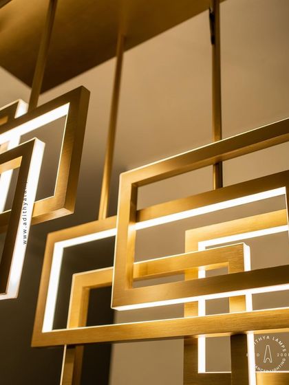 A multi-layered chandelier composed of intersecting rectangular frames with a brushed gold finish. The integrated LEDs cast a warm, ambient light, creating a dynamic and architectural statement piece for modern interiors.