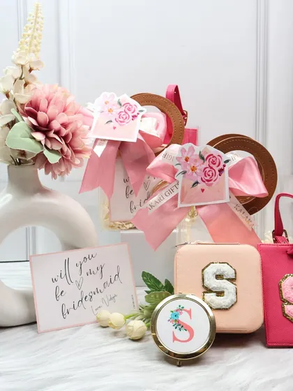This bridesmaid hamper in a delicate pink theme includes a personalized jewelry organizer, luggage tag, and pocket mirror. It's a thoughtful way to ask your friends to be part of your special day.
