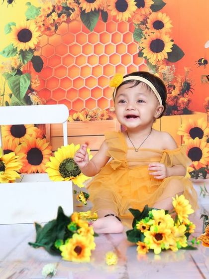 A happy baby girl laughs and plays in the sunflower and honeybee setup. Her joyful expression is the highlight of this bright and cheerful photoshoot.