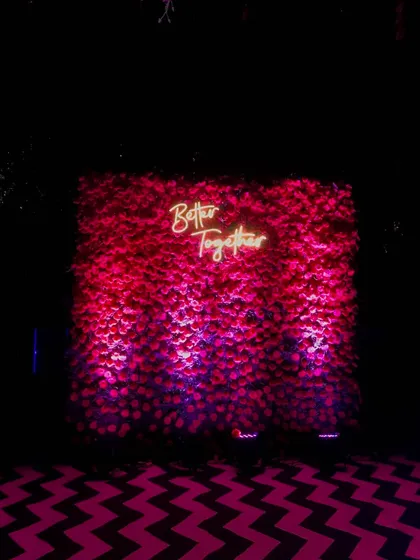 To add a modern touch to a party, I can create a dense flower wall like this one made of red roses. The custom neon sign makes it a perfect photo booth for guests.