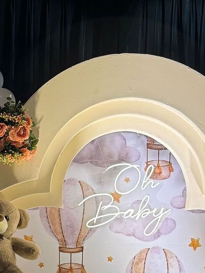 A close-up of the 'Oh Baby' neon sign and hot air balloon printed backdrop, framed by an elegant arched structure.