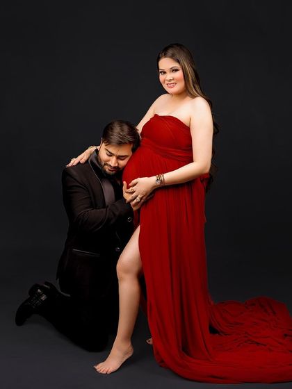 A classic and adoring pose with the dad-to-be listening to the baby bump. The vibrant red gown makes a bold and beautiful statement against the dark backdrop.