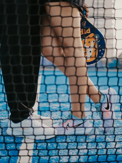 An artistic close-up of the couple's feet and a racket, seen through the court net, focusing on the details of the theme.