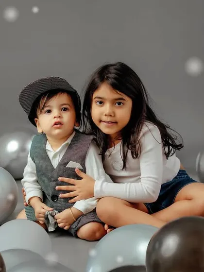 A sweet moment between siblings. The simple grey background and monochrome balloons create a modern and stylish sibling portrait.