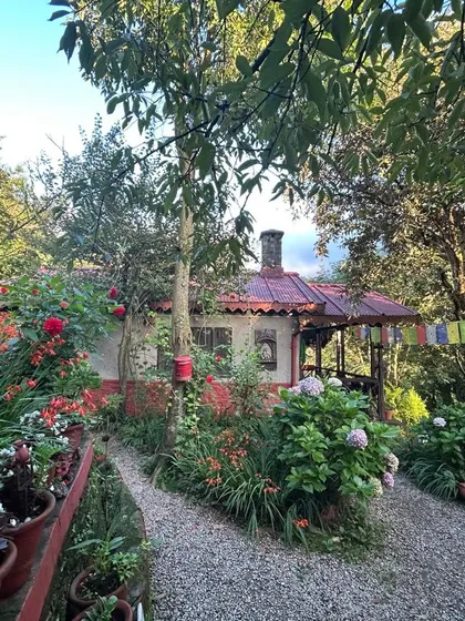 A cozy cottage at Jungle Lore Birding Lodge, surrounded by a vibrant garden and prayer flags. We offer a peaceful retreat where you can connect with nature and enjoy warm hospitality.
